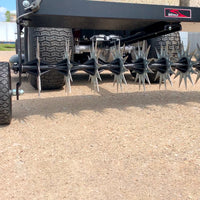 Close-up view of the Brinly Parts 40 Tow-Behind Spike Aerator (SAT2-40BH-P) on concrete. The spiked wheels enhance soil penetration for better airflow and nutrient absorption, promoting a healthier lawn root system. It features an extra-strength double tow bar and is attached to a black frame.