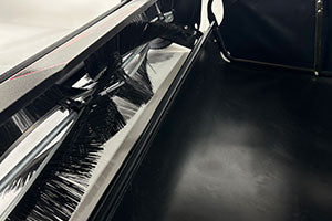 Close-up of a black, glossy interior of a vehicle or machinery component, featuring a reflective surface and a gear-like component on the left. The surroundings appear sleek and industrial.