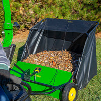 A green John Deere 42 Tow-Behind Lawn Sweeper (LPSTS-42JD / STS-42JD) with a high-capacity hamper, filled with dry leaves and attached to a tractor, sits on a grassy lawn near trees.