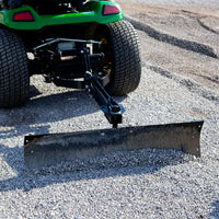 A green tractor with large tires is shown from behind, equipped with a Brinly Parts 42” Sleeve Hitch Box Scraper (BS-42BH), smoothing a path of small gravel stones on a wide gravel surface.