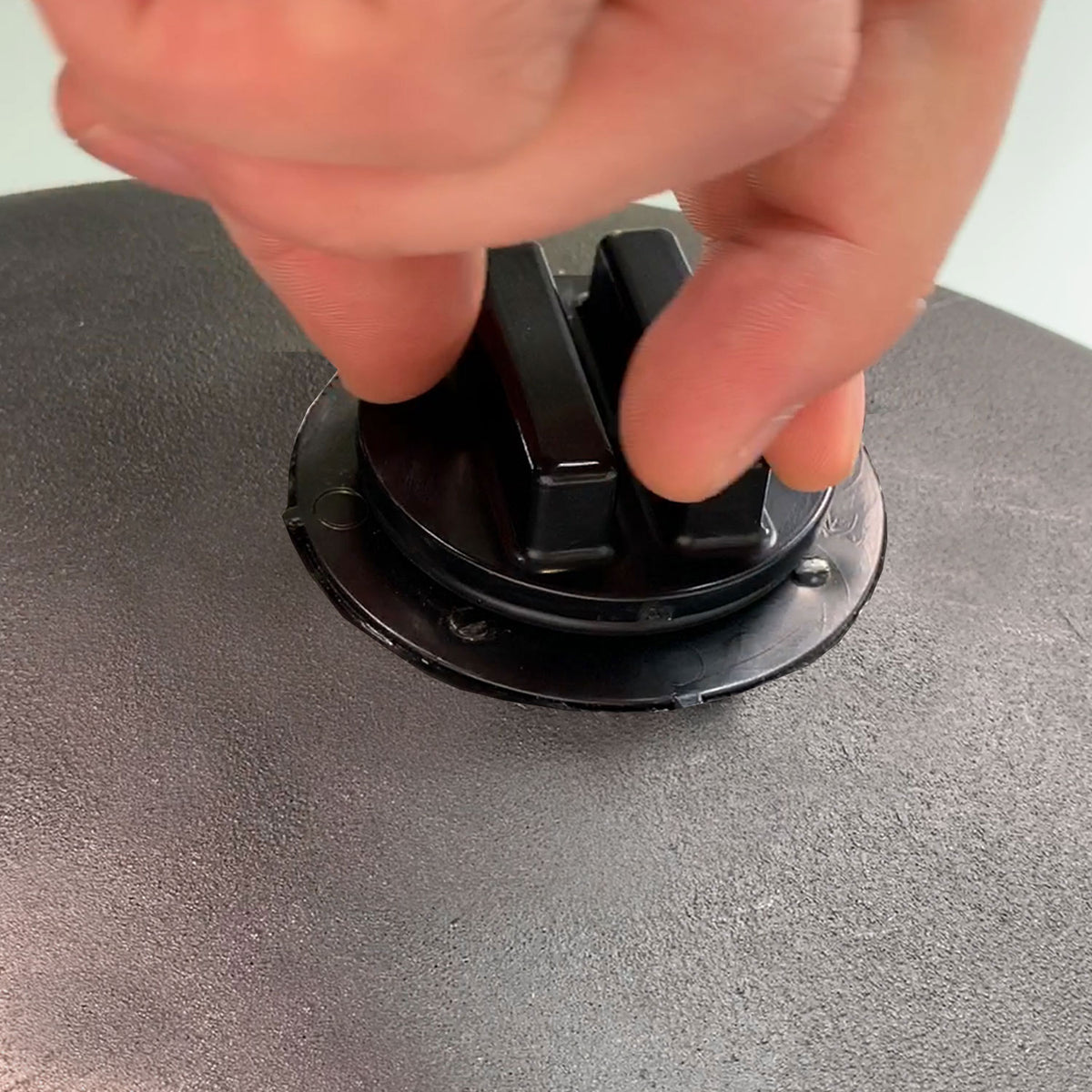 A hand adjusts a black plastic knob on the textured surface of the Brinly Parts 28 Gallon Push or Tow Poly Lawn Roller | PRC-242BH, suggesting interaction with its tow-behind mechanism.