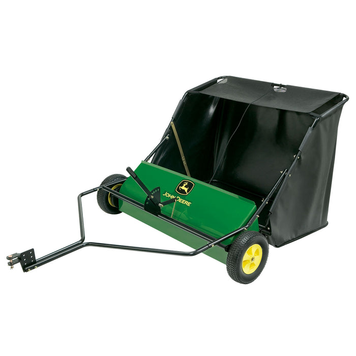 The John Deere 42 Tow-Behind Lawn Sweeper features green and black colors, yellow wheels, a sturdy tow bar, and a high-capacity hamper with a rotating brush mechanism. The brand name is prominently displayed on the front.