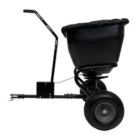 The image shows a Brinly Parts 175 LB. Tow-Behind Deluxe Spreader (BS361BH-A) with a black, rust-proof polyethylene bucket and extended handle. It features a universal hitch and sturdy tires for easy attachment to vehicles or lawn tractors, captured from the side view.