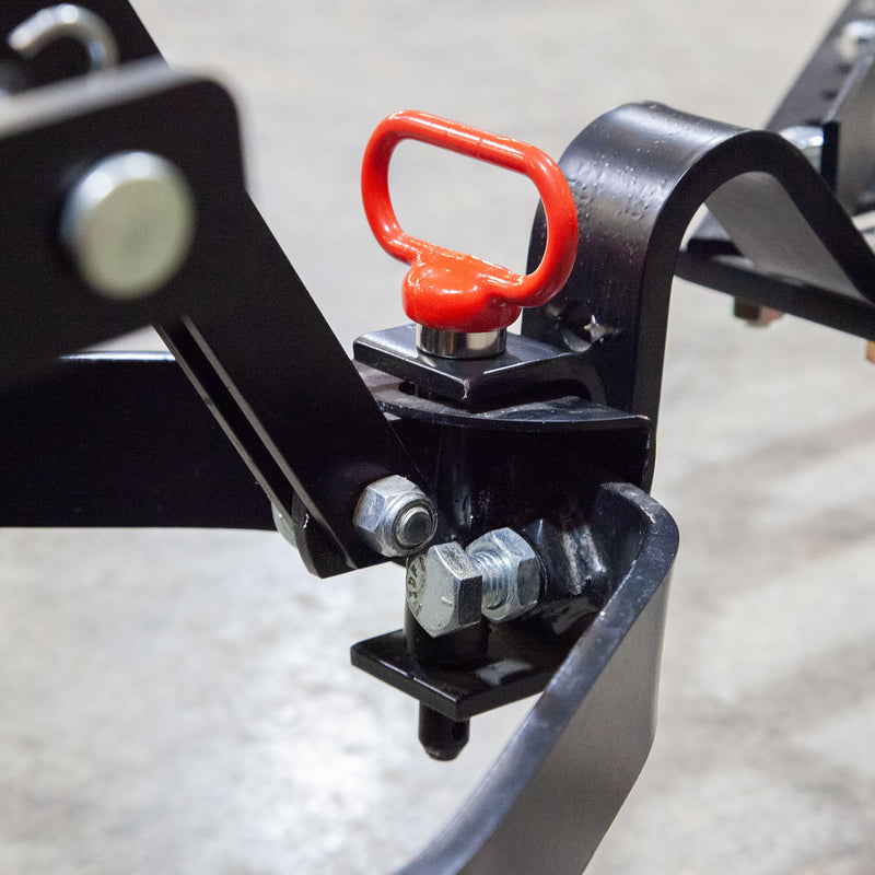 A close-up of a Brinly Parts Magnetic Hitch Pin (5/8 Inch) with bolts and a red pull handle, attached to a black frame on a gray floor—perfect for securing tow-behind lawn equipment.