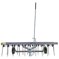 The Brinly Parts 40″ Dethatcher in Hammered Gunmetal (DT2-40BH-S) features black spring tines, two wheels, and a long vertical handle. Its silver frame has warning labels and can be attached to lawn mowers or tractors for effective moss and thatch removal.