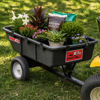 A Brinly Parts 10 Cu. Ft. Poly Cart (PCT-101BH), filled with potted flowers, green plants, and bags of brown mulch, sits on green grass attached to a yellow lawn tractor.