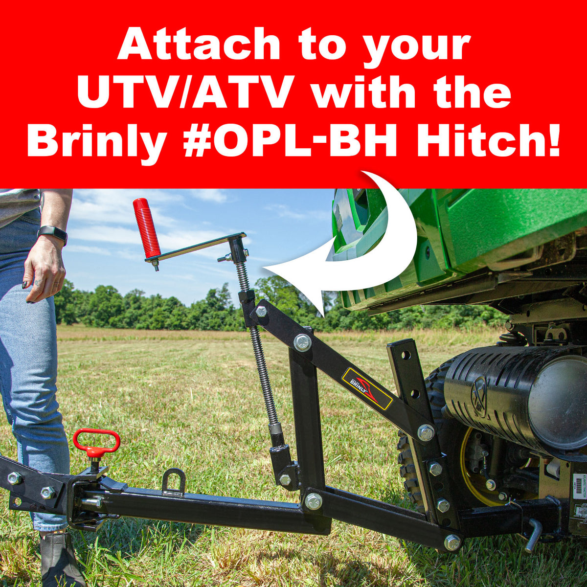 A person stands by a green UTV/ATV, attaching a Brinly Parts Sleeve Hitch Moldboard Plow | PP-510 with a red handle. The image focuses on the hitchs attachment feature, designed for tractors, set against a scenic grassy outdoor backdrop.