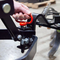 A close-up of a hand gripping the red latch handle of a Brinly Parts Magnetic Hitch Pin (5/8 Inch) on black metal machinery, with bolts and curved metal parts visible.