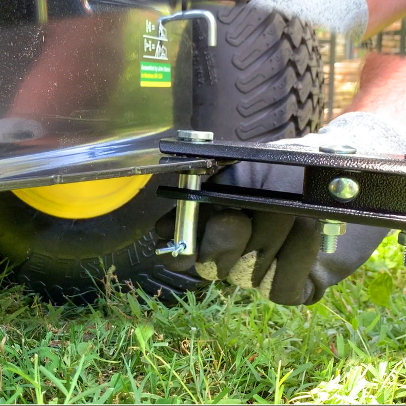 A person in black gloves tightens a bolt on the black metal bracket of a Brinly Parts 40″ Tow-Behind Dethatcher | DT2-40BH-G near its yellow wheel using a wrench, with grass clippings on the ground suggesting recent dethatching activity.