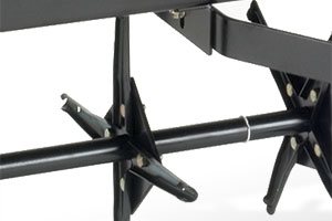 Close-up of a black metal aerator tool with spiked wheels designed for lawn care. The spikes are attached to a horizontal bar, used to penetrate soil for aeration.
