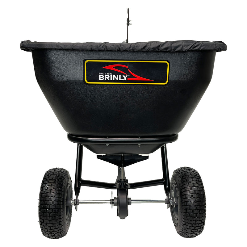 A black Brinly Parts 175 LB. Tow-Behind Deluxe Spreader (BS361BH-A) with two large rugged wheels, a fitted hopper cover, and a visible metal frame and axle, viewed from the rear.