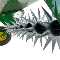 A close-up of the John Deere 40 Spike Aerator showcases sharp galvanized steel stars on a green frame. A small wheel featuring a yellow center is partially visible in the background, contrasting against a white backdrop.