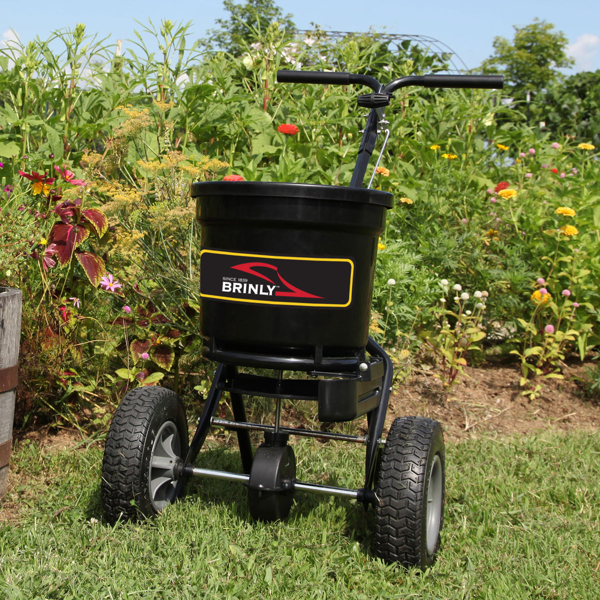 The Brinly Parts 50 LB. Push Spreader with Side Deflector & Hopper Cover (P20-500BHDF-A2) stands in the garden, ready for any spreading job.