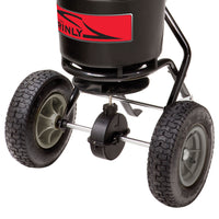 Close-up of the Brinly Parts 50 lb. Push Spreader (P20-500BH) shows its wheels and axle. The black plastic hopper with a red label is visible, and the large tires are mounted on a metal frame for easy movement across lawns, designed to evenly distribute fertilizer.