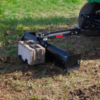 The Brinly Parts 42” Sleeve Hitch Box Scraper (BS-42BH), featuring a black carbon steel blade, is effectively clearing grass and soil when attached to green equipment like a tractor.