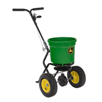 The John Deere Broadcast Spreader - 50 lb Round features a durable poly hopper with green and yellow accents, plus two large wheels and a handlebar for easy maneuvering, making it ideal for efficiently spreading seed or fertilizer on your lawn.