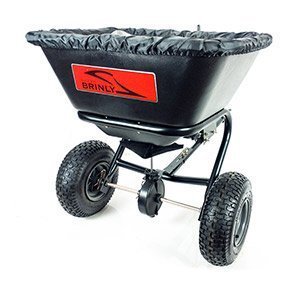 A black lawn spreader with large, textured wheels and a red brand logo on the side. It features a hopper with a protective cover and sturdy metal frame.