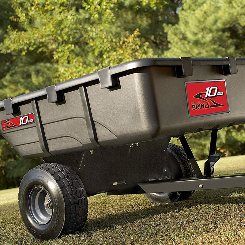 A black Brinly Parts 10 Cu. Ft. Poly Cart (PCT-101BH) with large wheels sits on grass outdoors, sunlight shining and trees in the background.