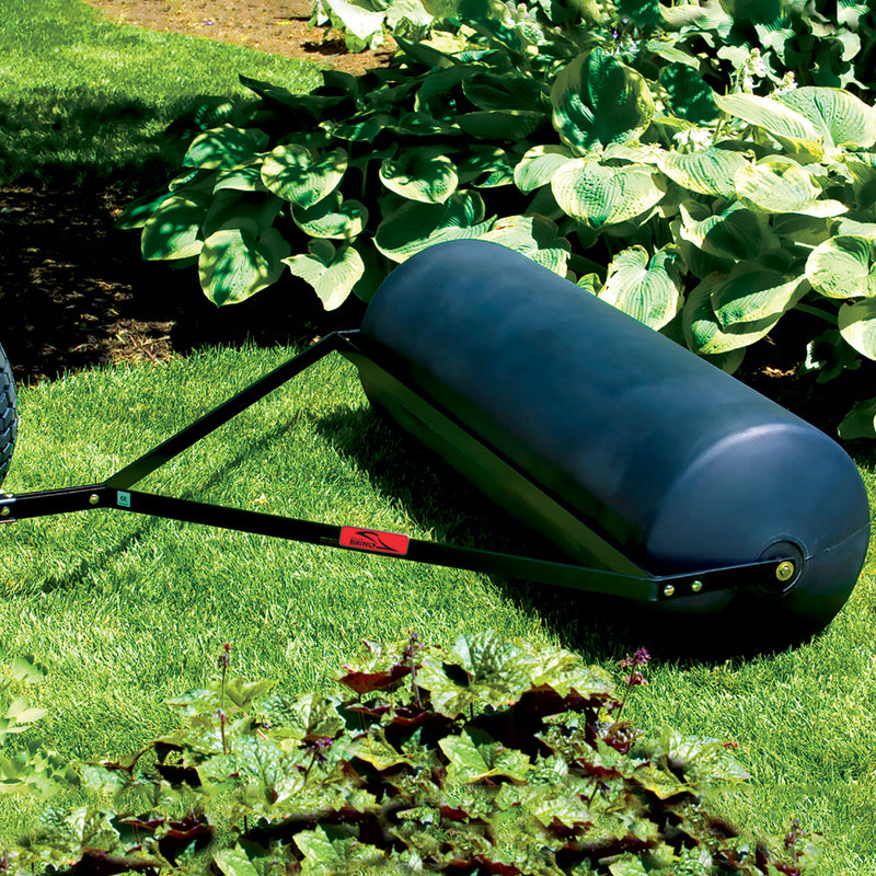 A Brinly Parts 54 Gallon Tow-Behind Poly Roller (PRT-482SBH), featuring a rust-free dark poly drum and metal frame, rests on lush grass, ready to perfect the lawn.