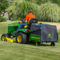 Wearing an orange shirt, a person rides a John Deere X730 equipped with the MC519 Material Collection System (LP49228) across a grassy lawn. The tractor, noted for its excellent hauling capacity, navigates effortlessly through swaying tall grasses.