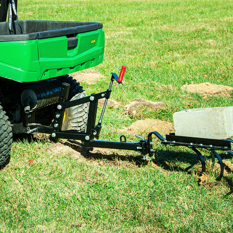 A green utility vehicle equipped with a Brinly Parts Universal ATV/UTV One-Point Lift for ground engagement hauls a small black plow stabilized by a cement block, perfect for tilling soil into freshly worked patches.