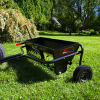 A Brinly Parts 40 Combination Aerator Spreader (AS2-40BH-G) with pneumatic tires sits on lush green grass. Equipped with spiked wheels perfect for lawn aeration, it stands out against a backdrop of lush trees and bushes under a clear sky.