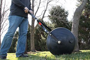 PRC 24BH feature 1 - 28 Gallon Push or Tow Poly Lawn Roller <span>|</span> PRC-24BH”>Spring is in the air, and it’s time to start working on your lawn. You may be laying down sod, planting grass seed, or smoothing down molehills. No matter which job, Lawn Rollers help you to get the lawn care chores done quickly and easily.

Lawn rollers are cylindrical “mini steam rollers” with added weight (usually water or sand) that help flatten the ground. You can choose a push lawn roller, which requires manual work to roll it across the yard. Alternatively, you can select a lawn roller attachment, which hooks to the back of your tractor and rolls behind you as you drive. While pull-behind rollers are typically more expensive, they do tend to get the job done faster and easier than a labor-intensive push roller. Rollers are typically constructed of either steel or poly, and come in a variety of weight capacities and sizes.
<h2>When to Use a Lawn Roller?</h2>
<ul>
 	<li><strong>For Sod:</strong> Before you sod, you can use a roller to ensure the ground is nice and flat. After removing existing vegetation, tilling, and adding fertilizer, you can roll over the ground to flatten it. You should keep this up until the ground is packed enough so that your feet don’t sink when you walk over it. After laying down the sod and watering it, use a roller to remove air pockets and press the sod down to ensure the roots make contact with the soil. This will help the sod establish itself and lead to better growth.
<header id=